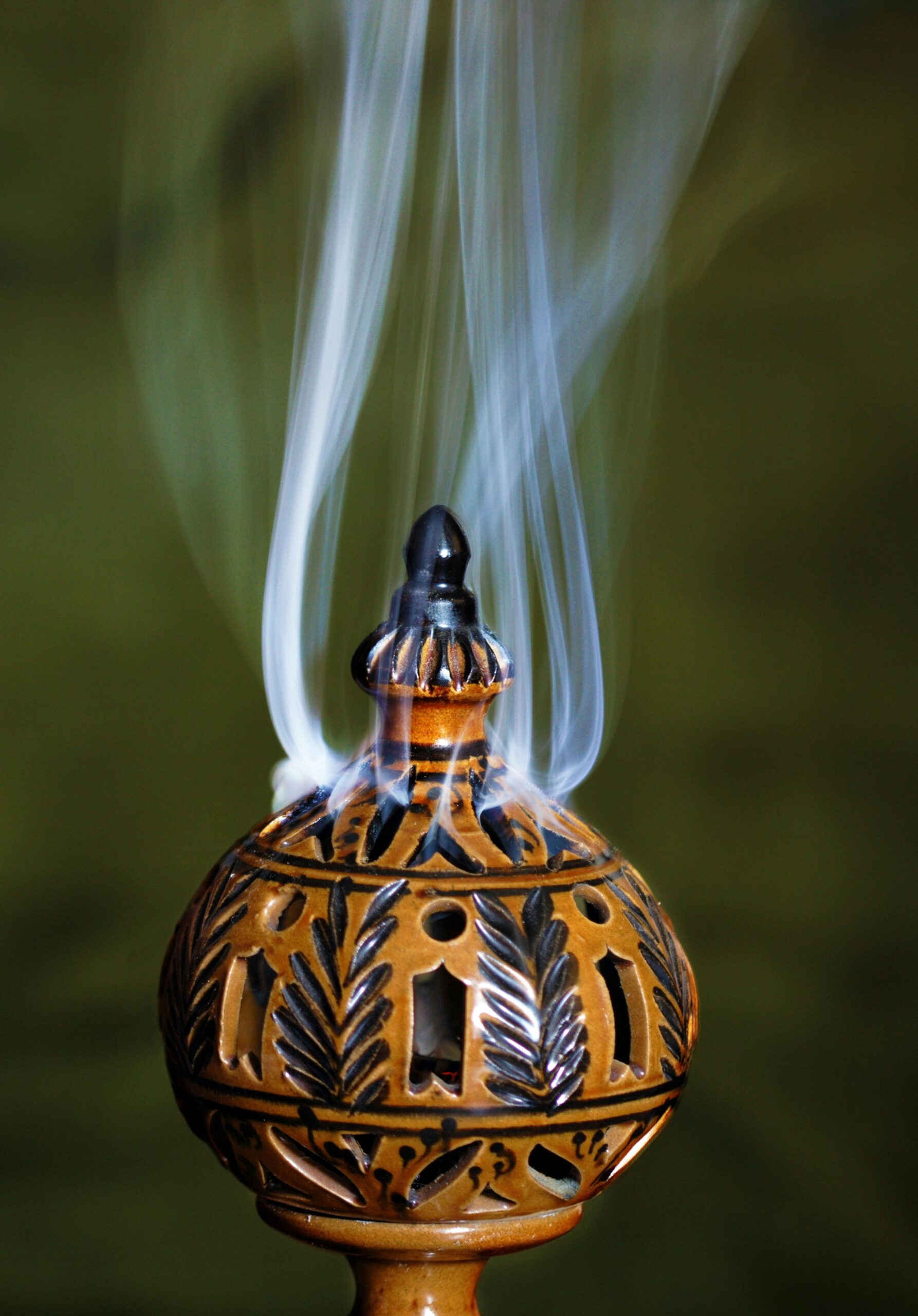 Elegant ceramic incense burner with intricate design and smoke rising against a green background.