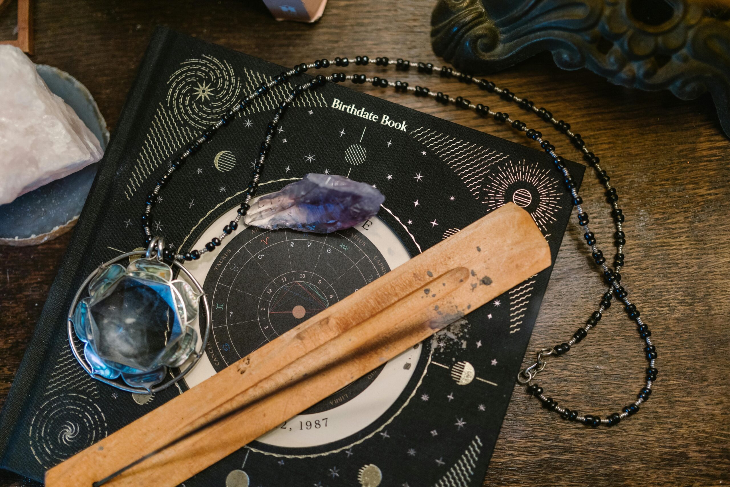 Astrology-themed flat lay featuring a birthdate book, crystals, and necklace on a wooden surface.