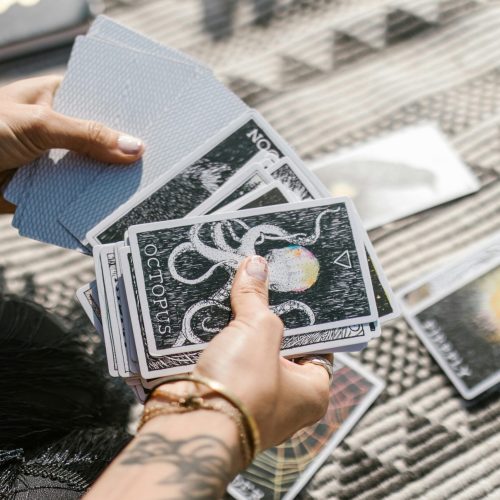 Hands holding tarot cards during a reading session on a patterned mat.